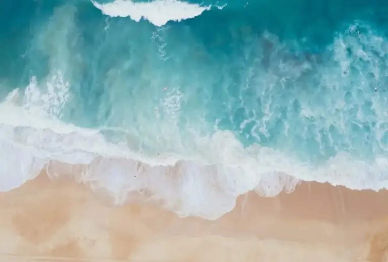 Vertical aerial view taken by a drone of waves on a beach with turquoise water