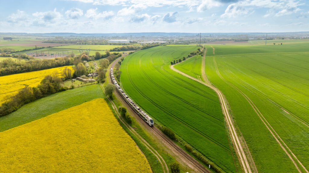 Vue aérienne par drone d'un train SNCF traversant un champ de colza sur la ligne Paris-Granville en Normandie