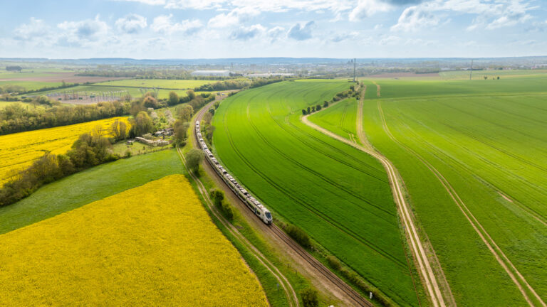 Vue aérienne par drone d'un train SNCF traversant un champ de colza sur la ligne Paris-Granville en Normandie
